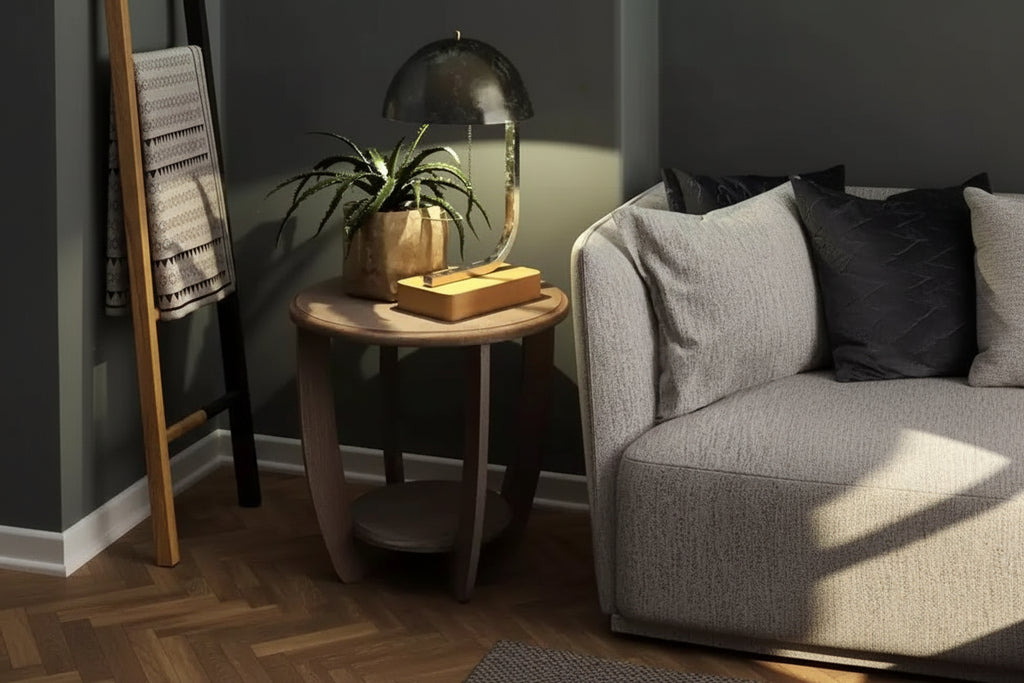 Wooden side table with lamp and plant next to a gray sofa in a dimly lit room.